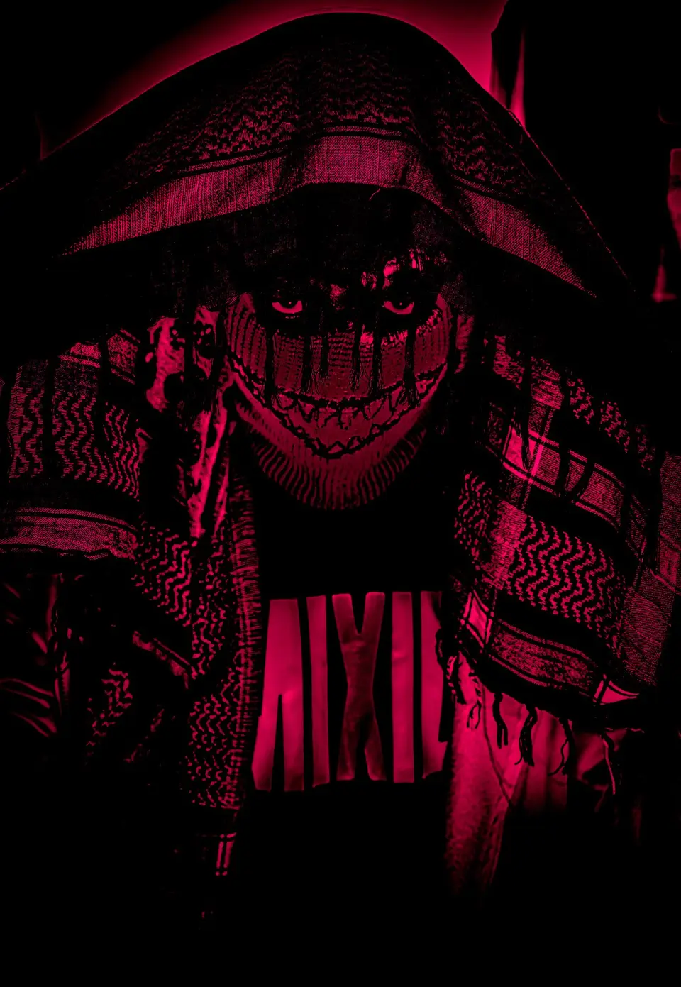 Person wearing a ski mask with embroidered teeth, under a keffiyeh, red light