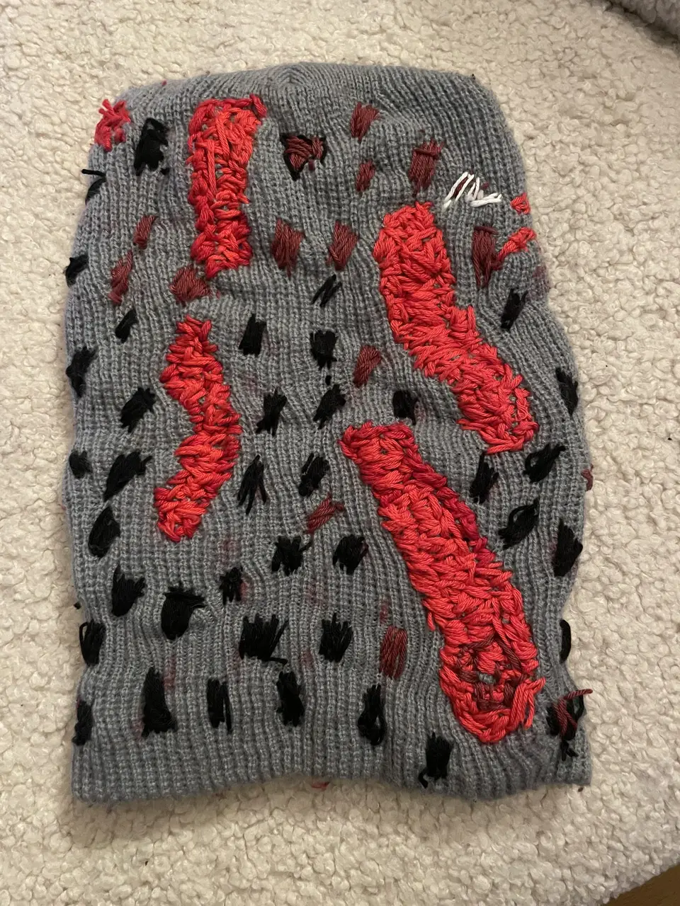 Back of ski mask Nº 7: looped raised red shapes and black hatching on gray knit